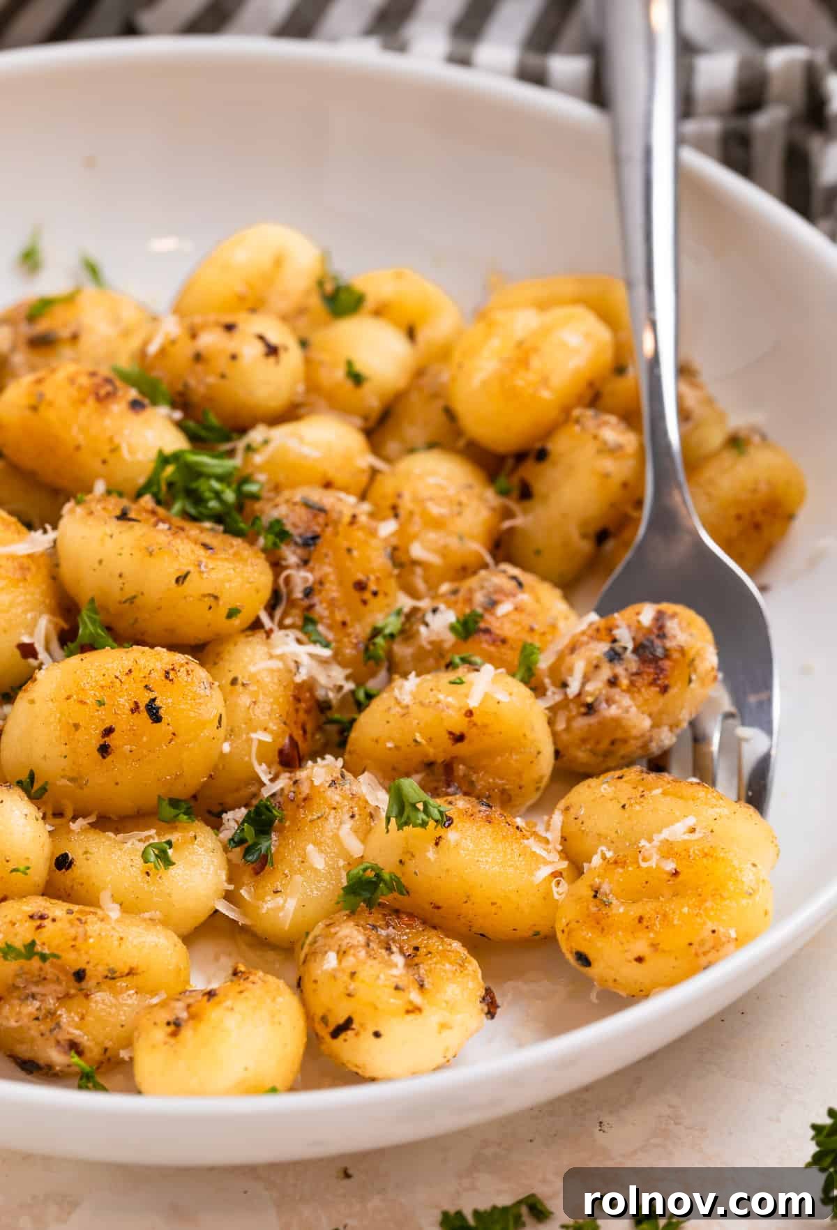 Golden Skillet Gnocchi 3 A white plate showcasing golden-fried gnocchi, generously topped with freshly grated Parmesan cheese and vibrant chopped parsley, ready to be enjoyed.