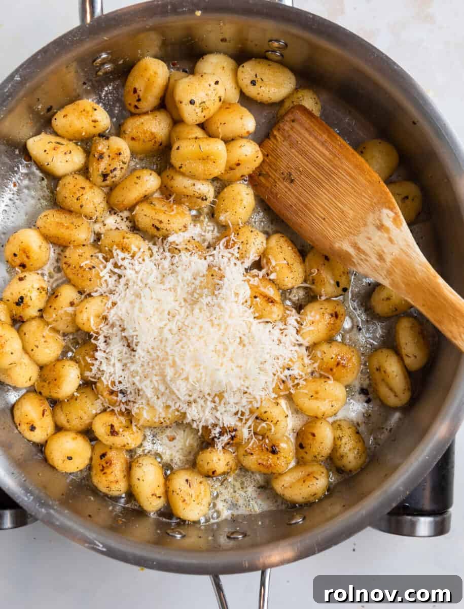 Golden Skillet Gnocchi 8 Freshly grated Parmesan cheese being stirred into a skillet of hot, pan-fried gnocchi with a wooden spatula.
