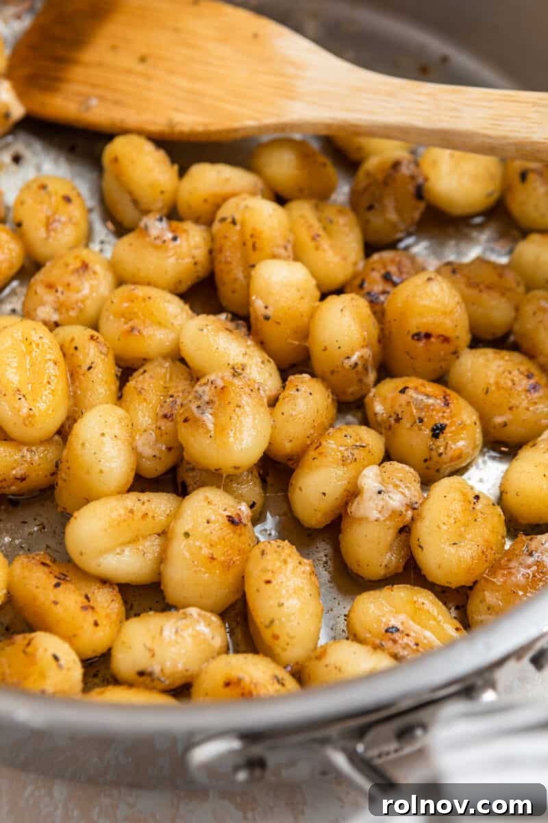 Golden Skillet Gnocchi 9 Finished pan-fried gnocchi, golden and seasoned, resting in a stainless steel skillet with a wooden spoon.