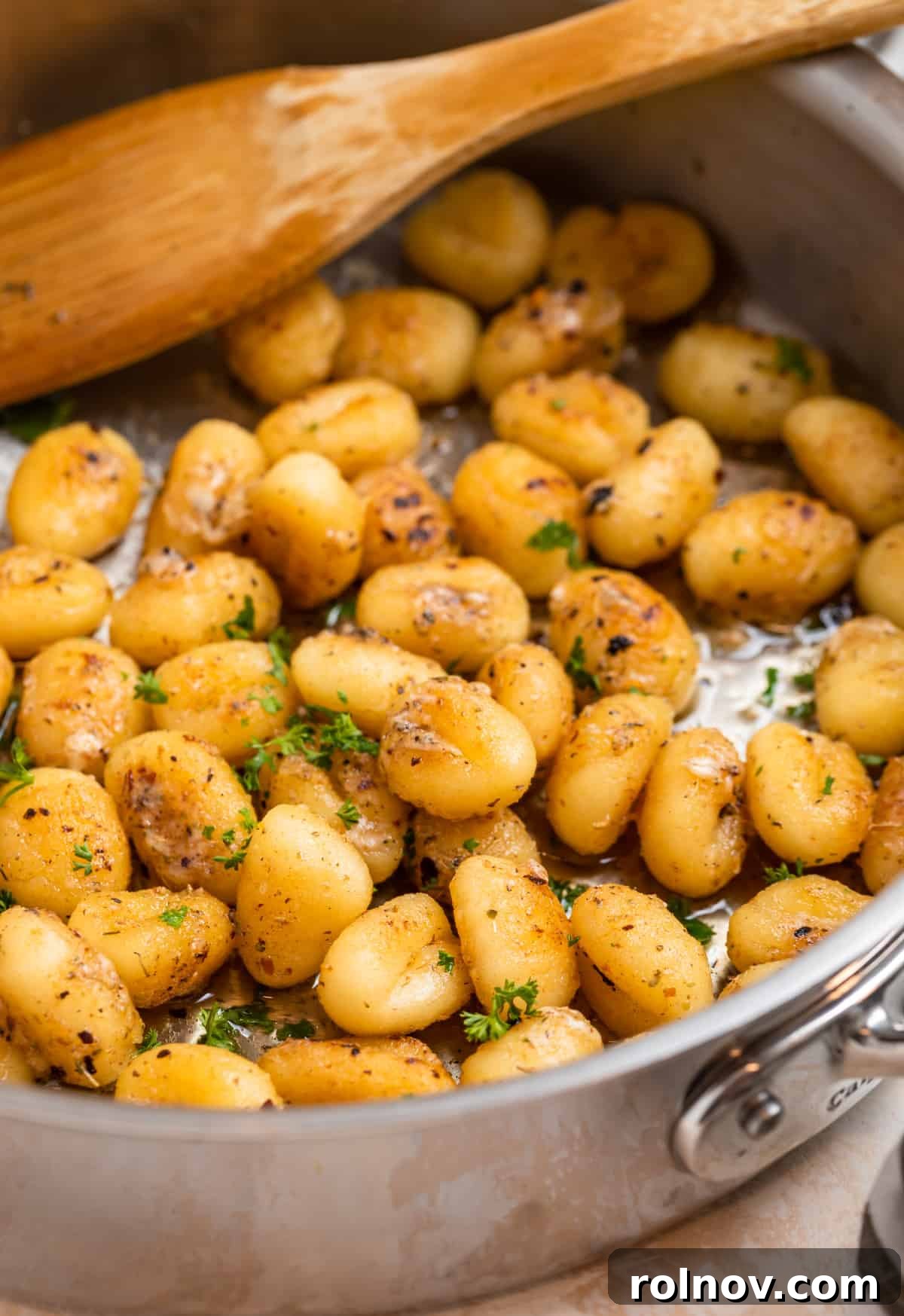 Golden Skillet Gnocchi 10 A vibrant close-up of pan-fried gnocchi in a skillet, coated in melted butter, adorned with grated Parmesan and freshly chopped parsley, ready to be served.