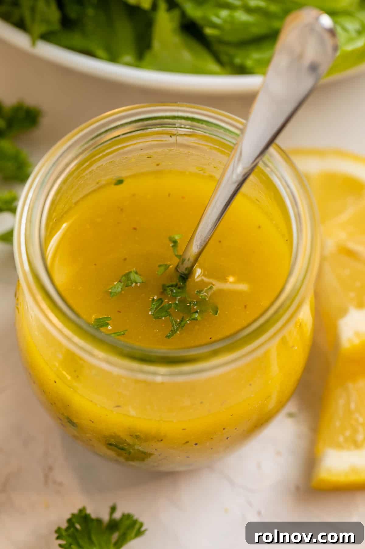 Honey lemon dijon dressing in jar topped with chopped parsley and spoon inside.