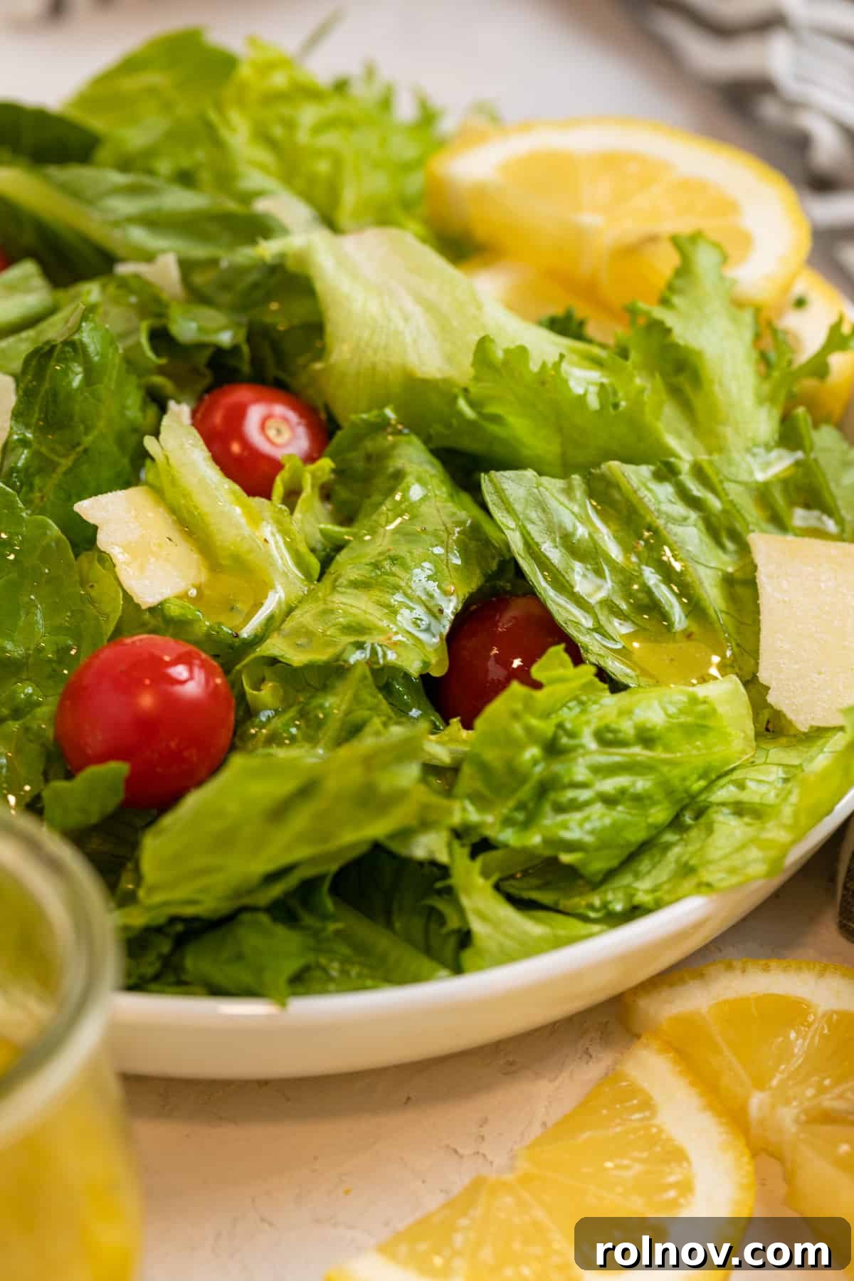 White plate with green salad topped with cheese and tomatoes as well as honey lemon dressing.
