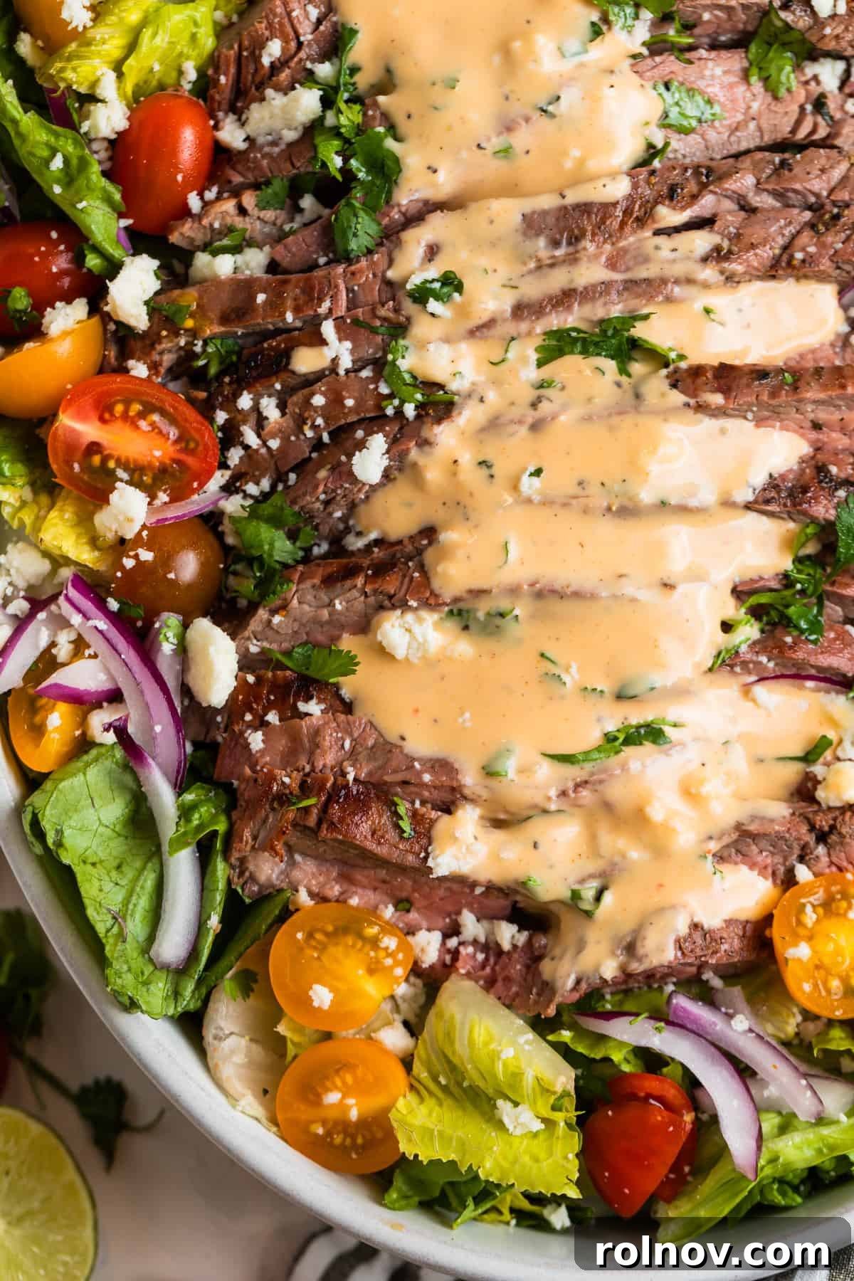 Powerhouse Flank Steak Salad 3 Grilled flank steak salad in a large bowl, drizzled with creamy sriracha dressing.