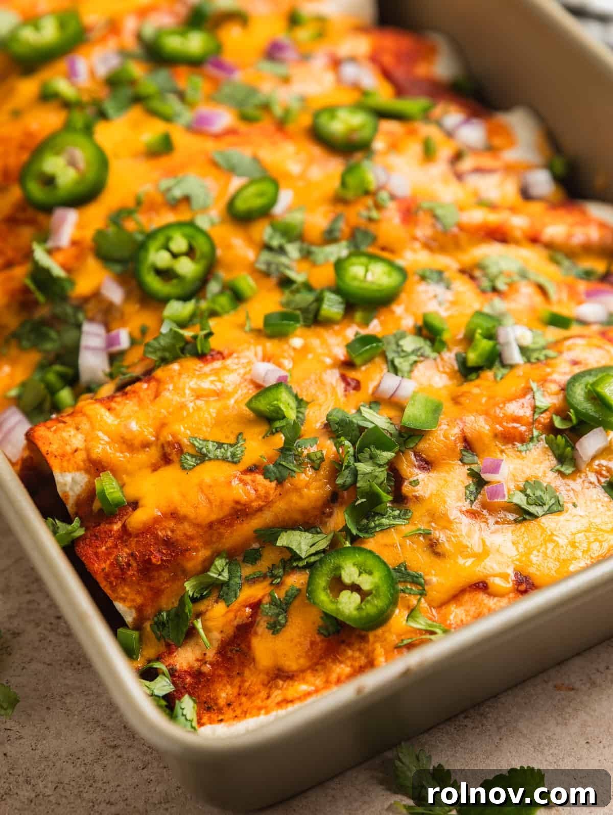 Enchiladas in pan topped with melted cheese and other toppings.
