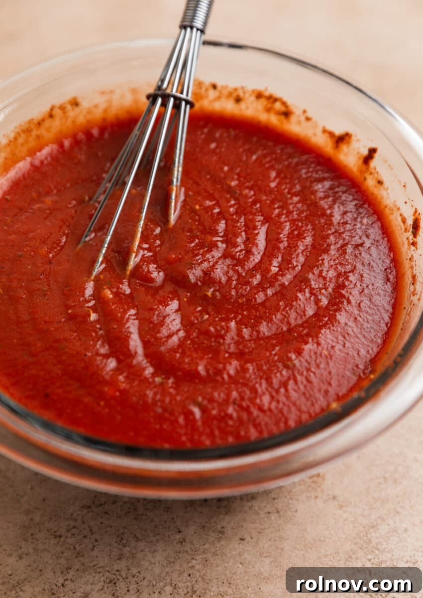Enchilada sauce in glass bowl with whisk.