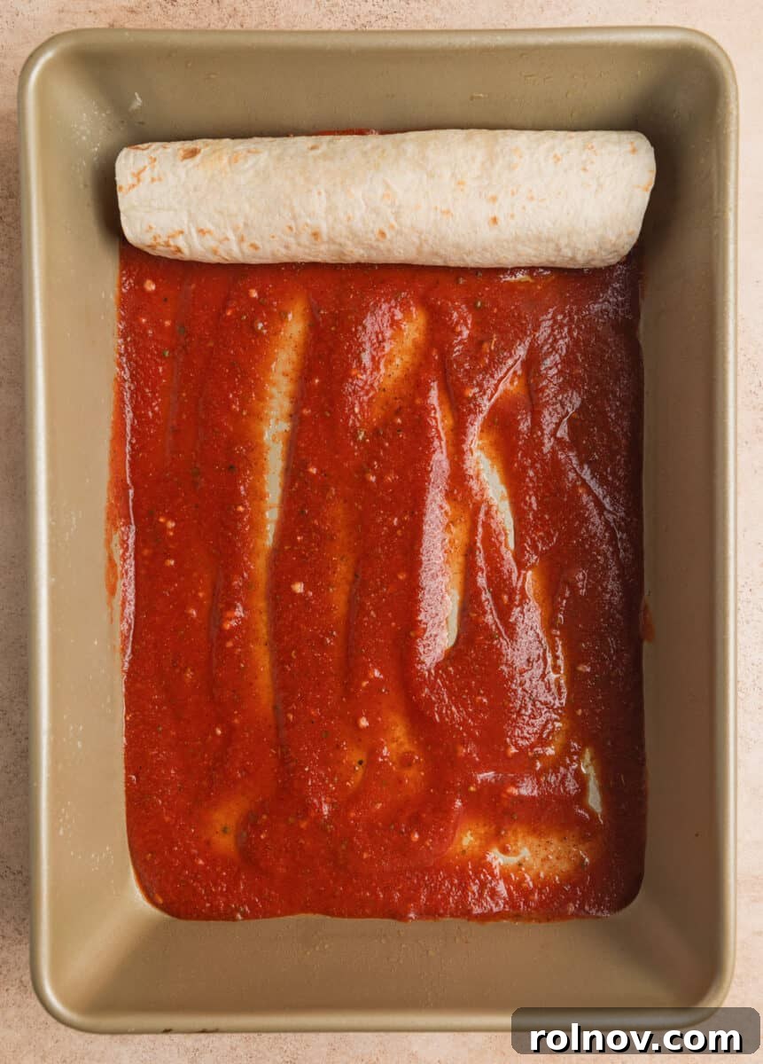 Rolled enchilada in pan with enchilada sauce on bottom of pan.