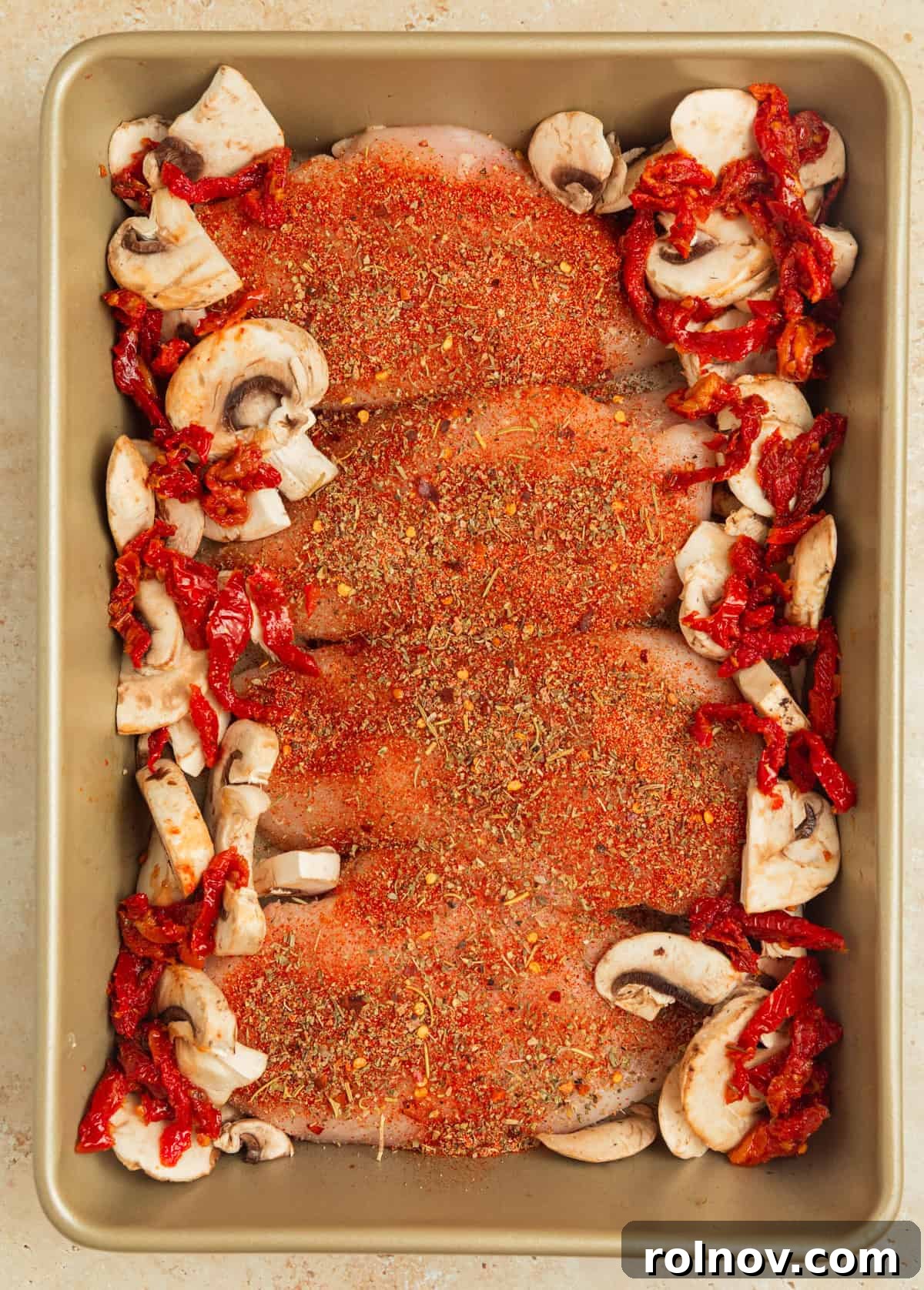 Savory Tuscan Chicken Bake 5 Baking pan with seasoned chicken, surrounded by vibrant sun-dried tomatoes and sliced mushrooms, awaiting the creamy sauce.