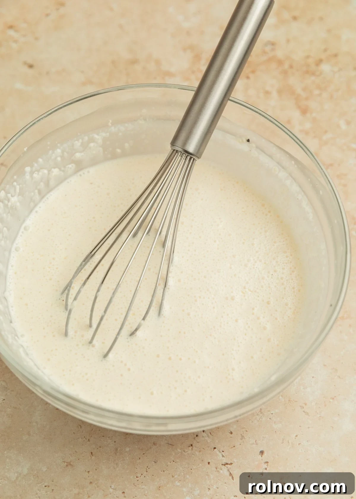 Savory Tuscan Chicken Bake 6 Smooth, rich cream sauce mixture in a glass bowl with a whisk, showing the perfect consistency before adding cheese.