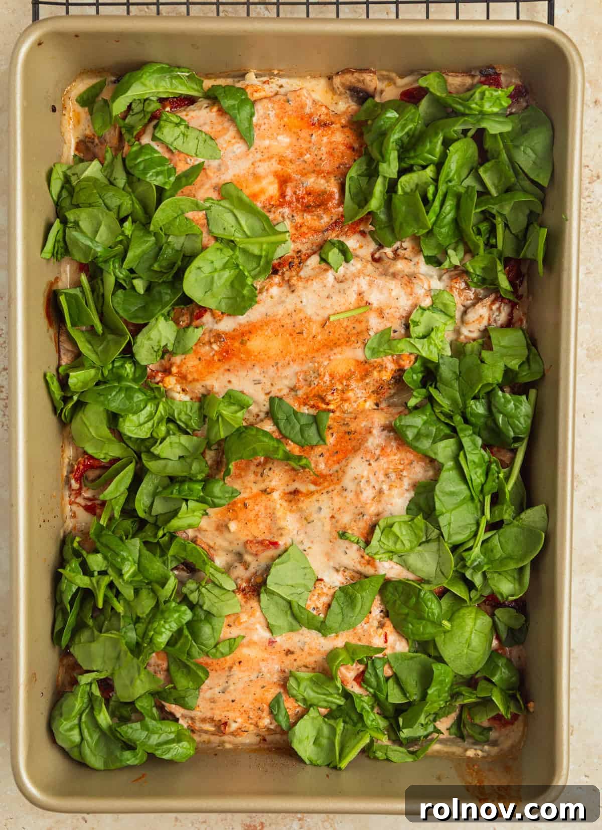 Savory Tuscan Chicken Bake 10 Finely chopped fresh spinach being added to the hot, creamy Tuscan chicken in the baking pan, ready to be stirred in and wilted.