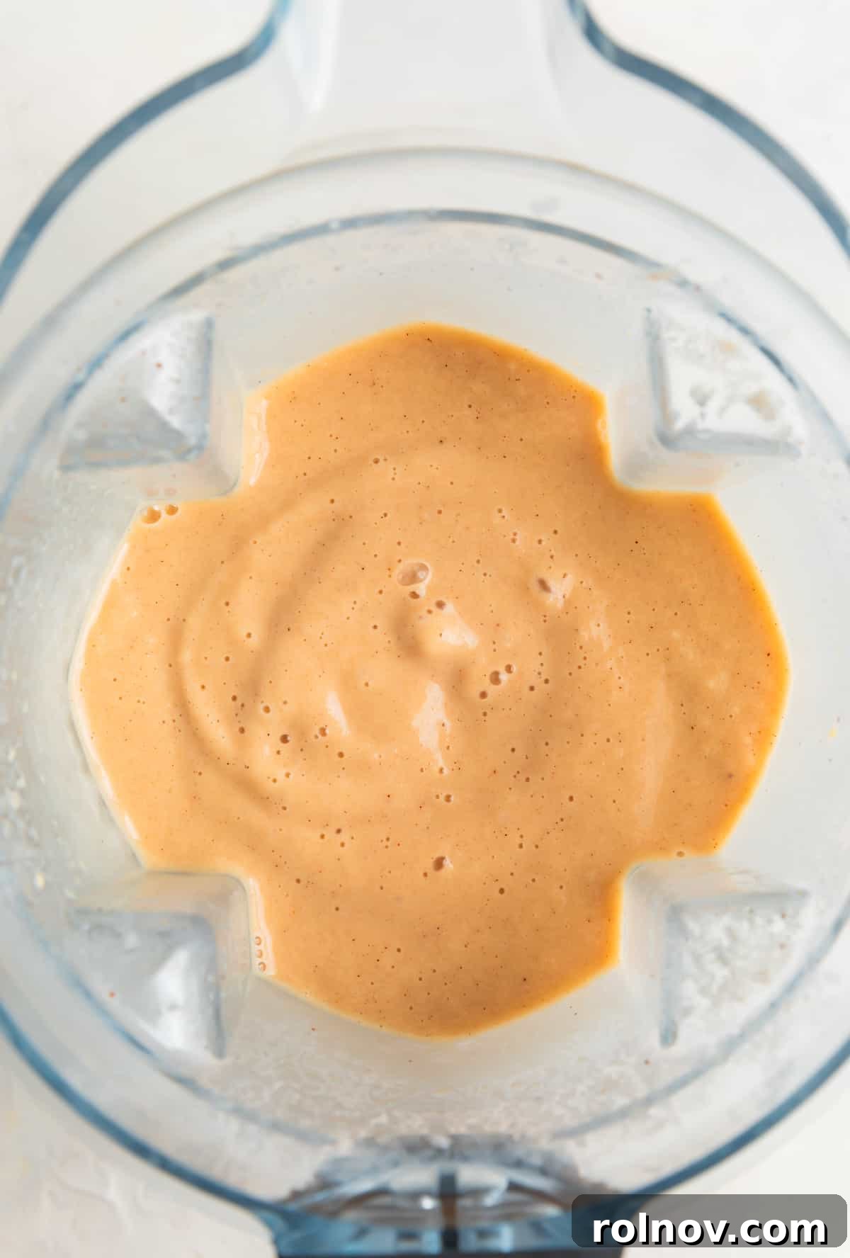 A blender filled with a perfectly smooth and creamy banana peach smoothie, showing the blended texture just before pouring.