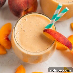Peach banana smoothie in glass with peach slices surrounding.