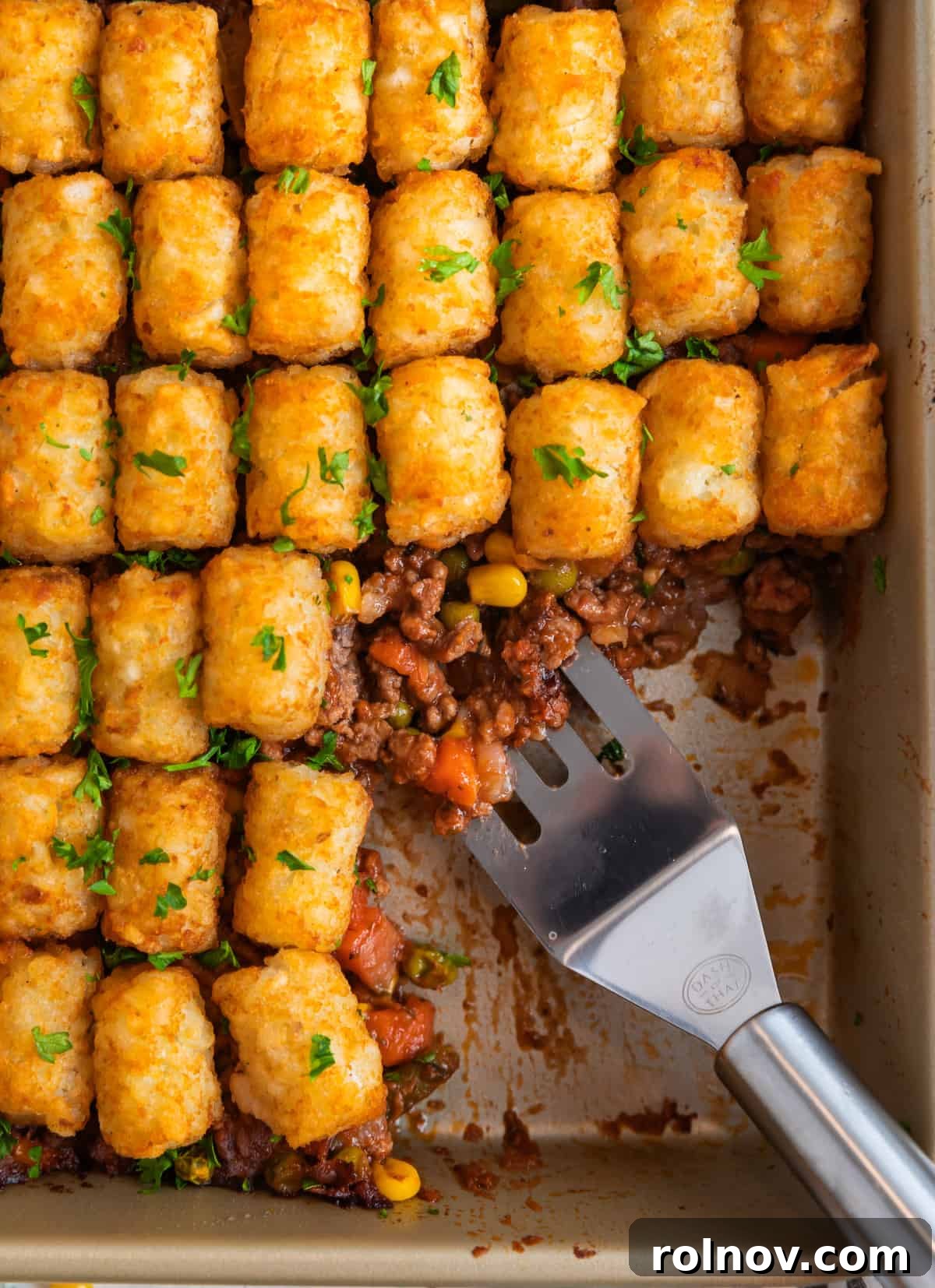 Shepherd's pie topped with tater tots in pan with spatula scooping out serving.