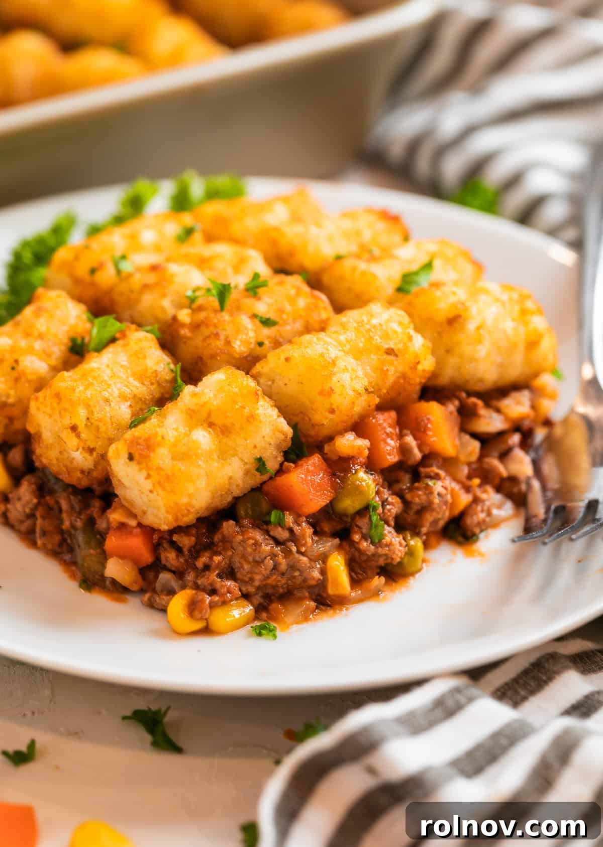 Tater tot shepherd's pie on white plate with fork and topped with chopped parsley.