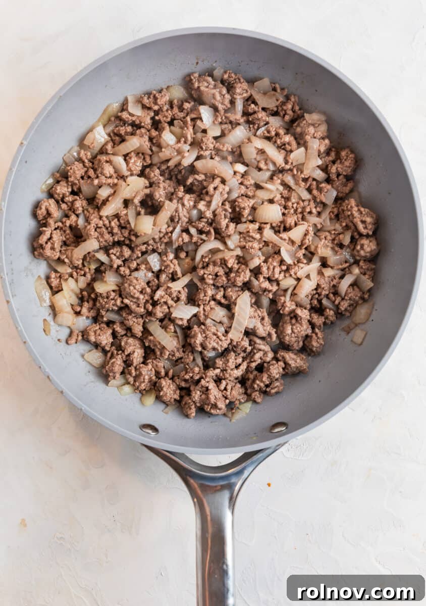 Ground beef and onions cooked in gray skillet.
