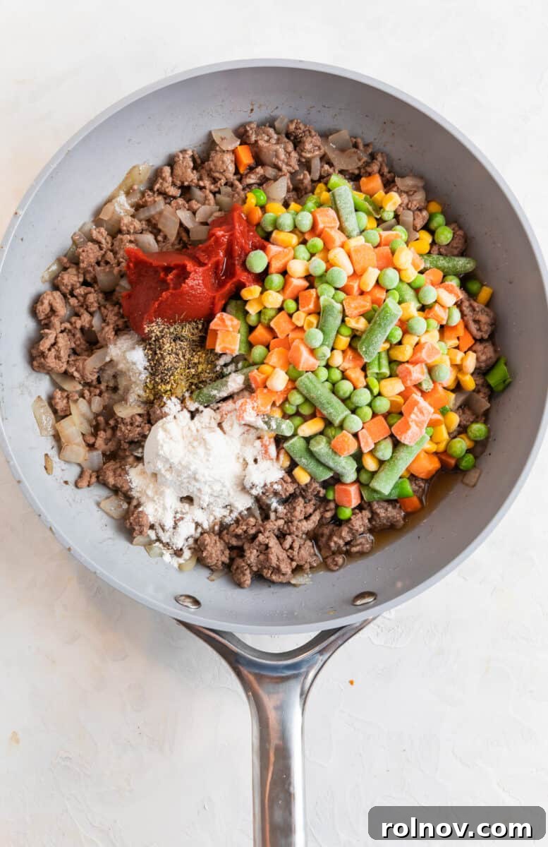 Frozen mixed vegetables, beef, tomato paste, corn starch and other ingredients in skillet.