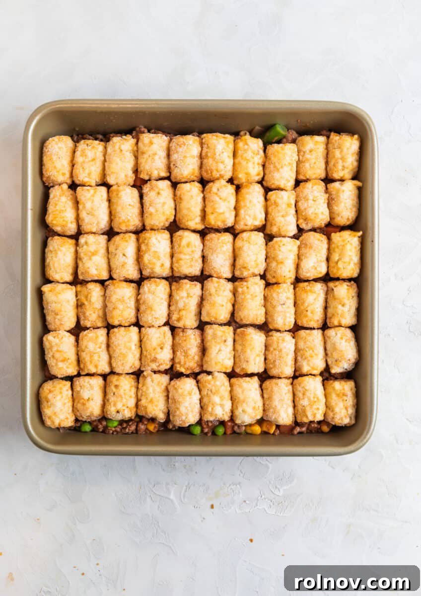 Tater tots lined over beef mixture in baking pan.