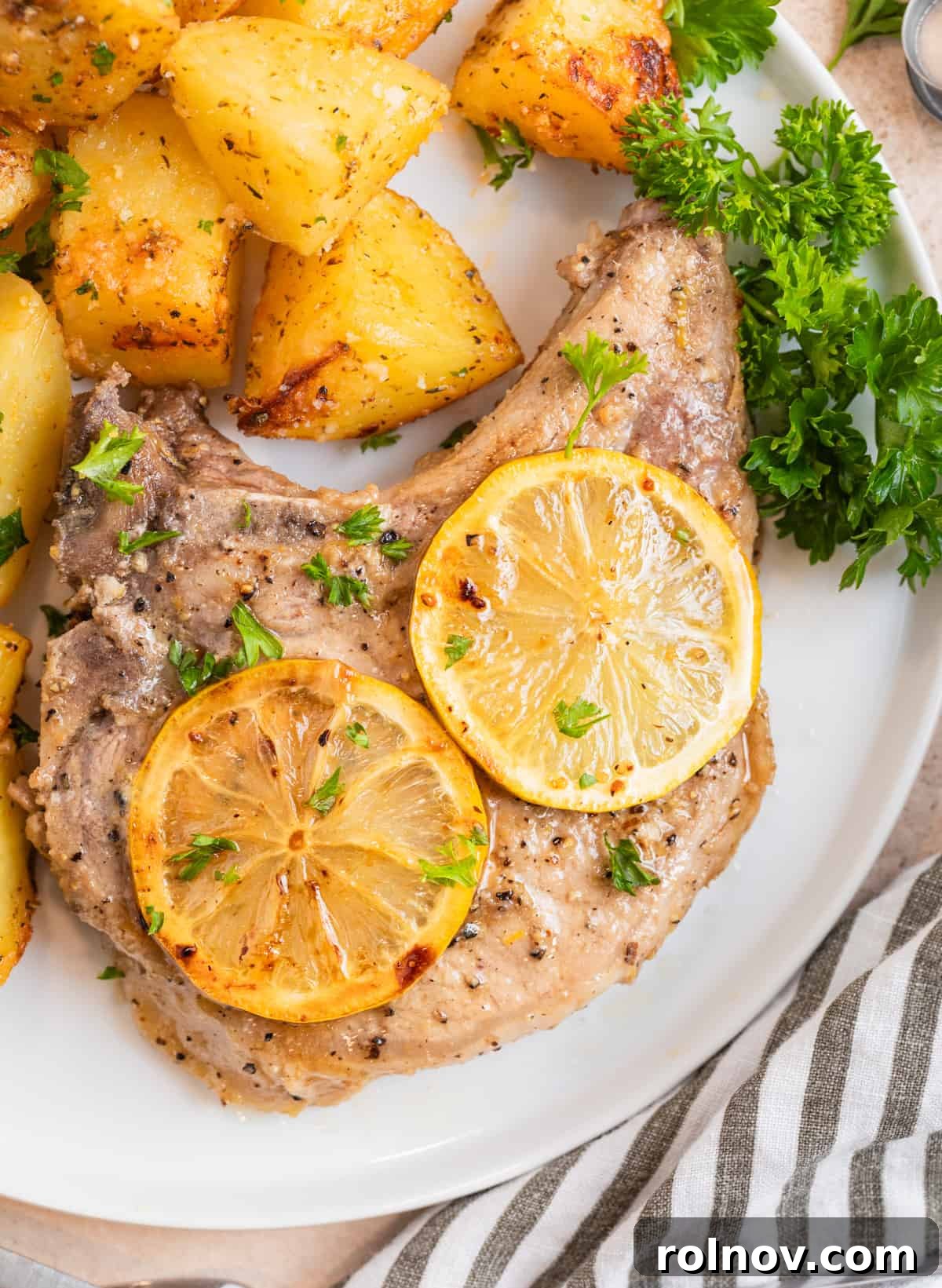 Zesty Lemon Pepper Pork Chops 2 A perfectly seared lemon pepper pork chop resting on a white plate, garnished with fresh parsley and roasted potatoes, ready to be enjoyed.