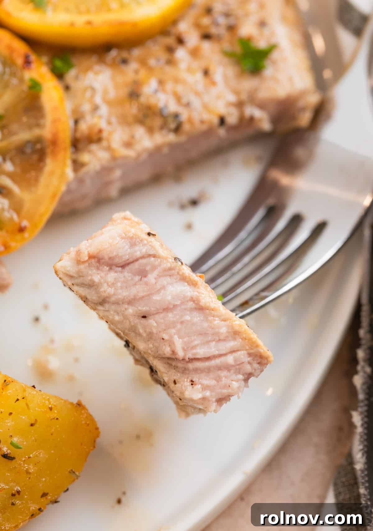 Zesty Lemon Pepper Pork Chops 3 A close-up of a fork holding a piece of juicy lemon pepper pork chop, highlighting its tender texture and golden crust.