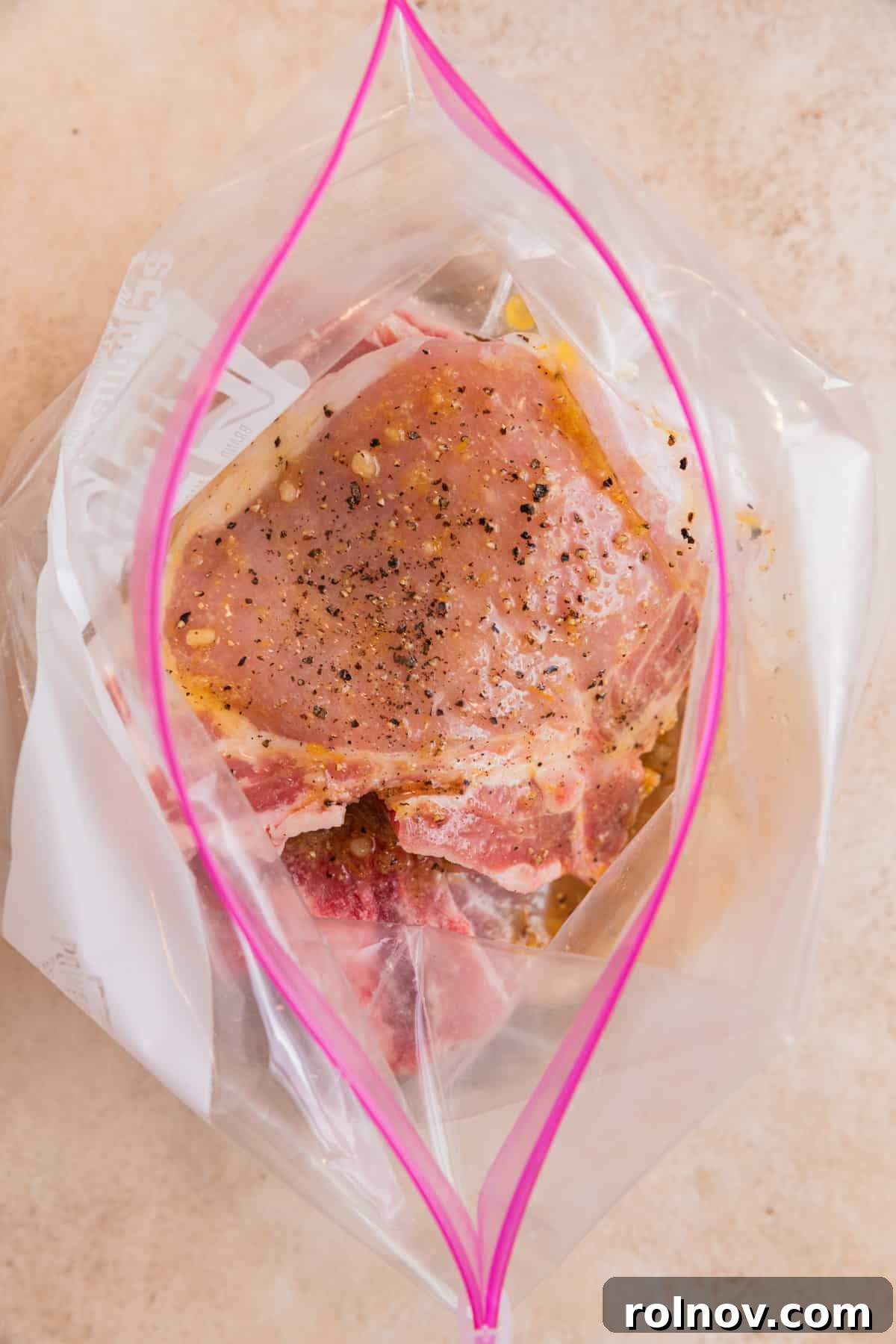Zesty Lemon Pepper Pork Chops 5 Raw pork chops submerged in the bright lemon pepper marinade within a sealed plastic bag, ensuring maximum flavor infusion.