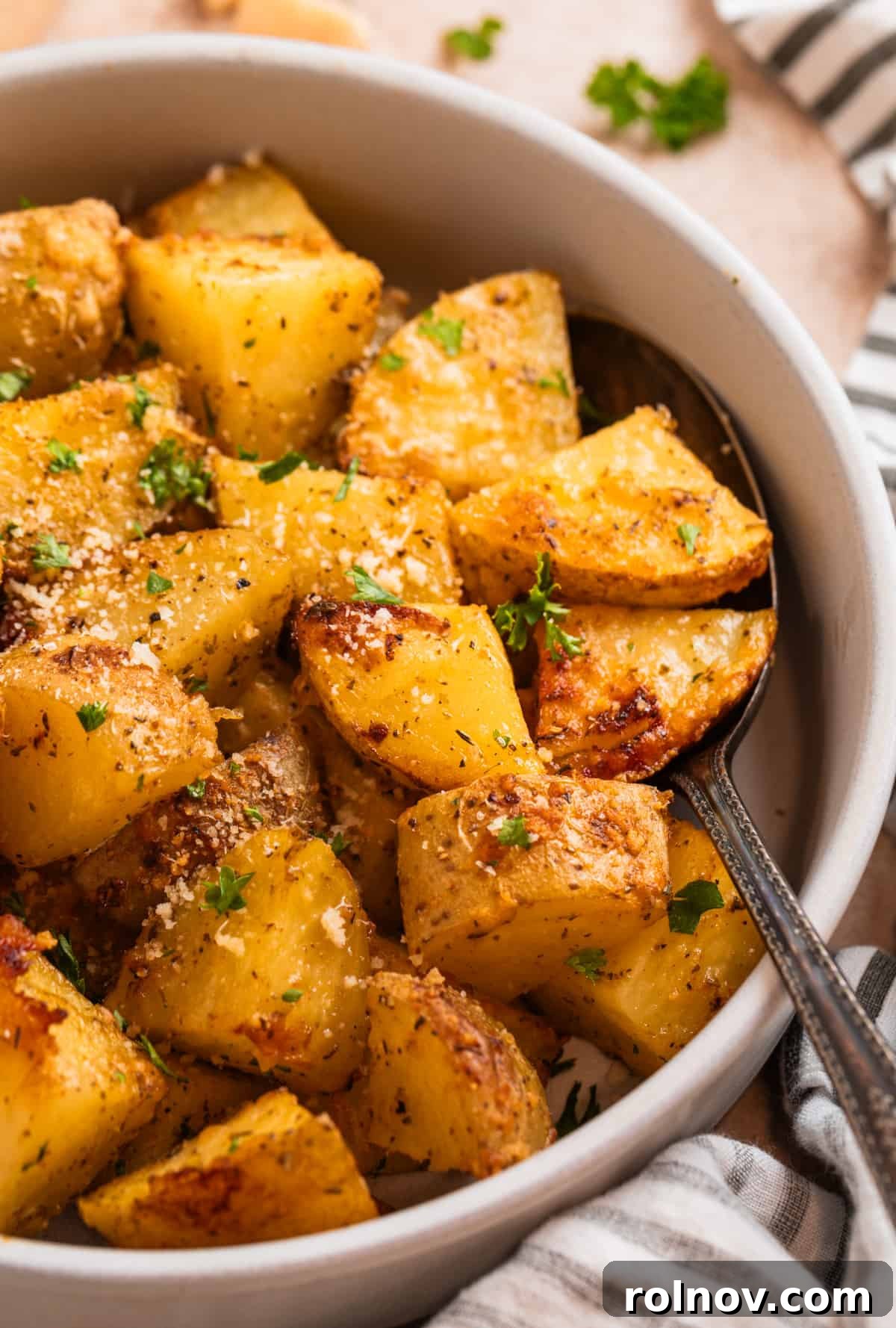 Crispy Parmesan Roasted Potatoes 2 Parmesan crusted potatoes in serving bowl with freshly grated parmesan and chopped parsley on top.