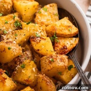 Crispy Parmesan Roasted Potatoes 9 Parmesan roasted potatoes in serving dish with spoon topped with chopped fresh parsley and freshly grated parmesan.