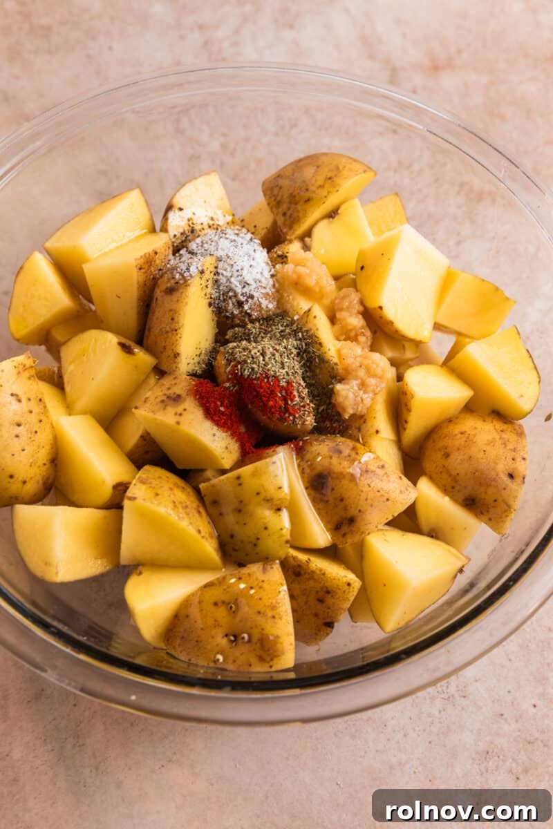 Crispy Parmesan Roasted Potatoes 4 Cubed potatoes in glass bowl with salt, pepper, garlic and other seasoning poured over top.