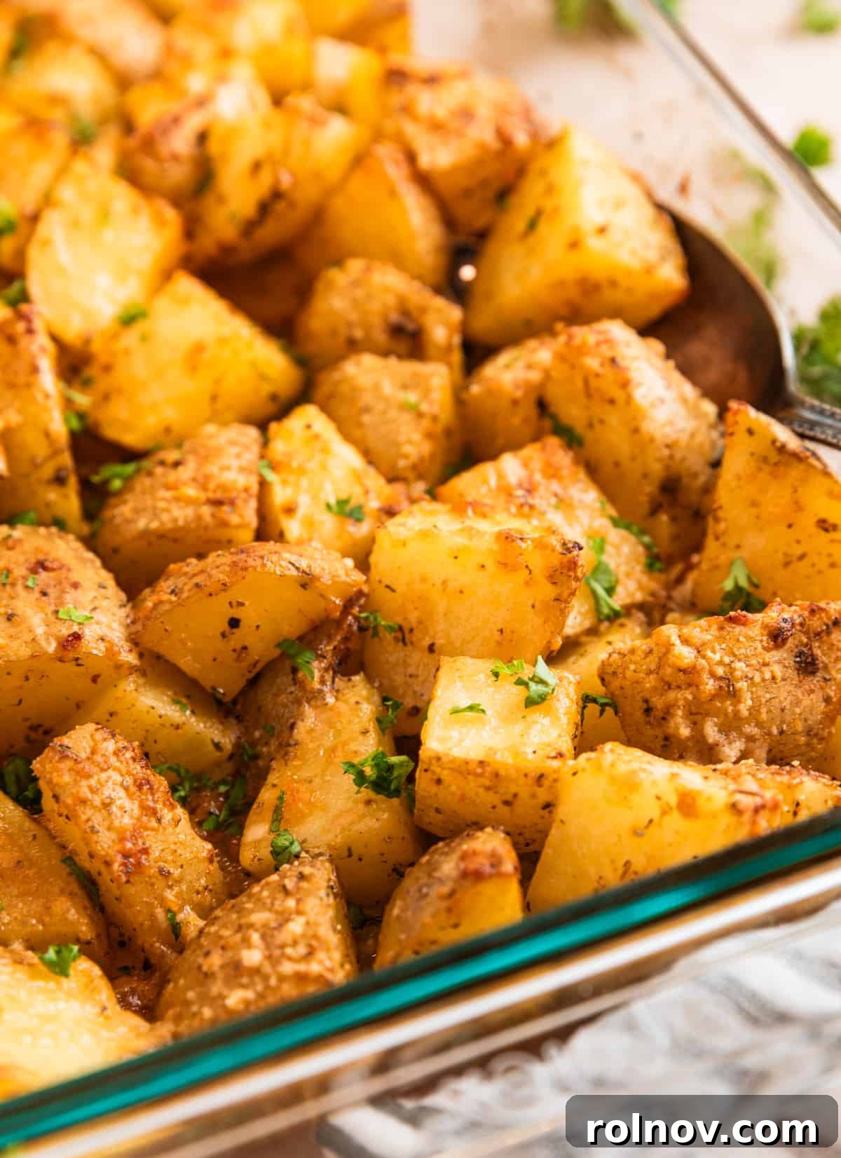 Crispy Parmesan Roasted Potatoes 8 Potatoes in pan with serving spoon topped with chopped parsley.