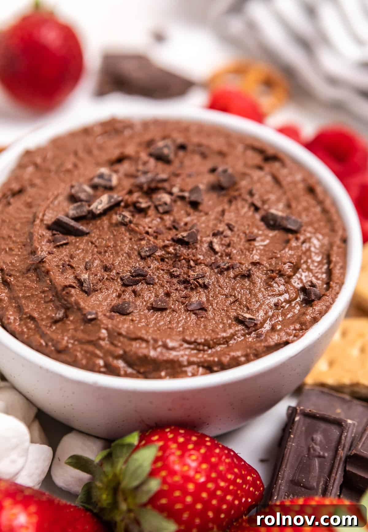 White bowl with brownie batter dessert hummus surrounded by berries and other dippers.