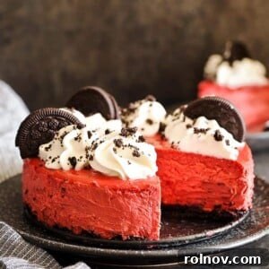 A decadent slice of Red Velvet Oreo Cheesecake with whipped cream and chocolate cookie crumbs.