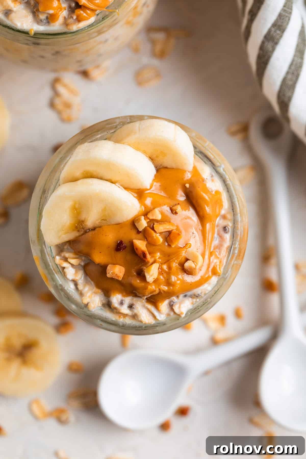 Power-Packed Overnight Oats 3 Overhead view of oatmeal topped with sliced bananas and peanut butter with white spoon and rolled oats surrounding.