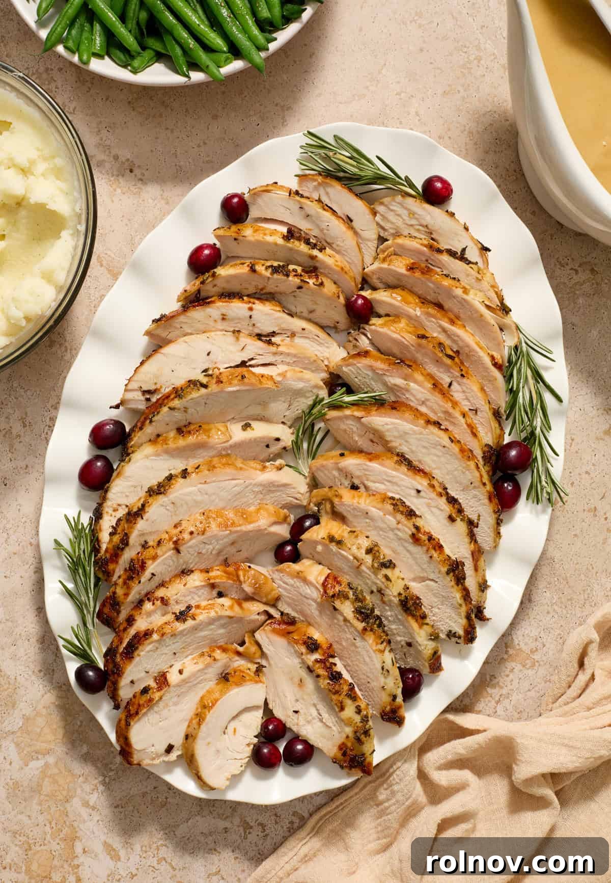 Sliced turkey breast on serving plate with rosemary and cranberry garnish.