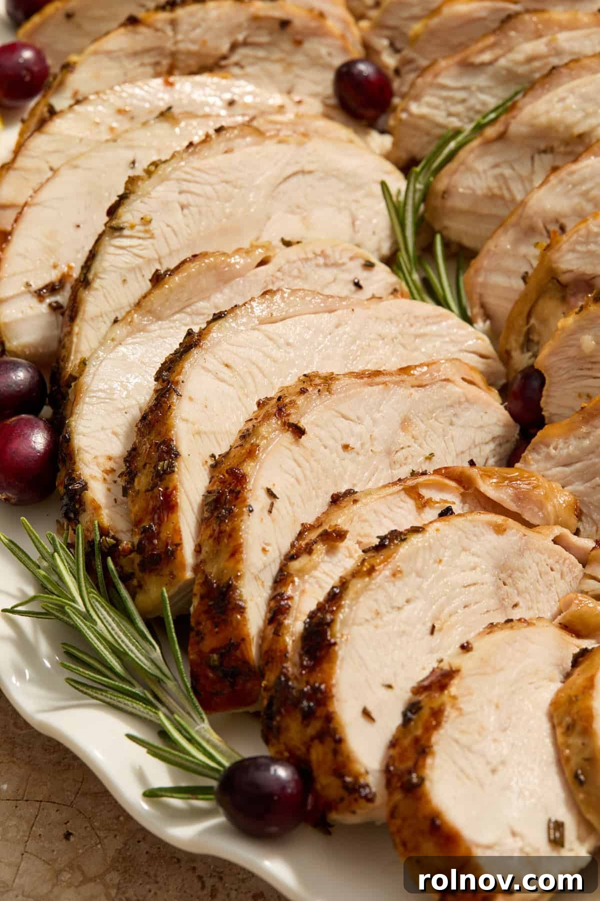Slices of turkey on serving platter with fresh rosemary and cranberries.