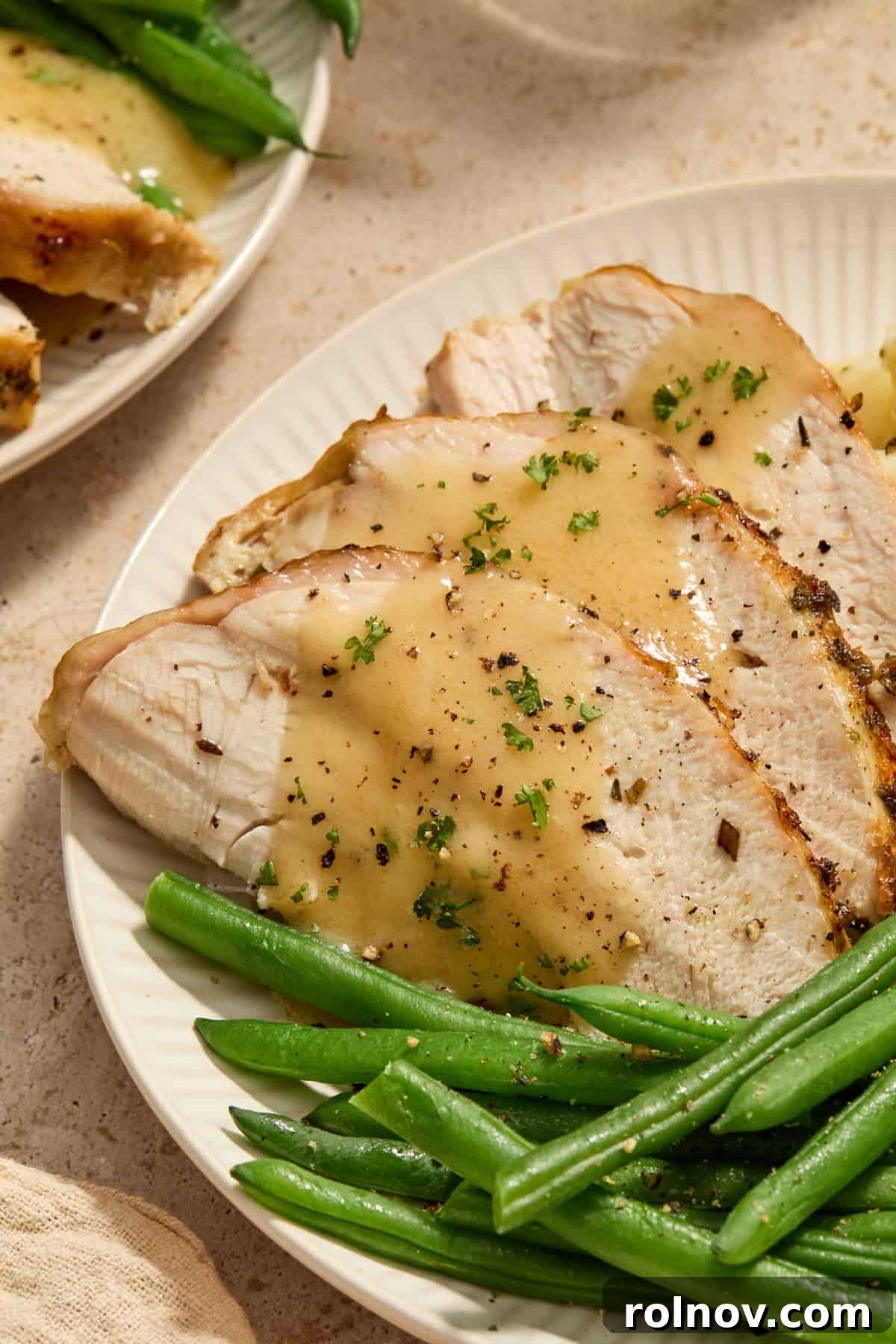 Sliced turkey breast on plate with green beans and gravy on top.