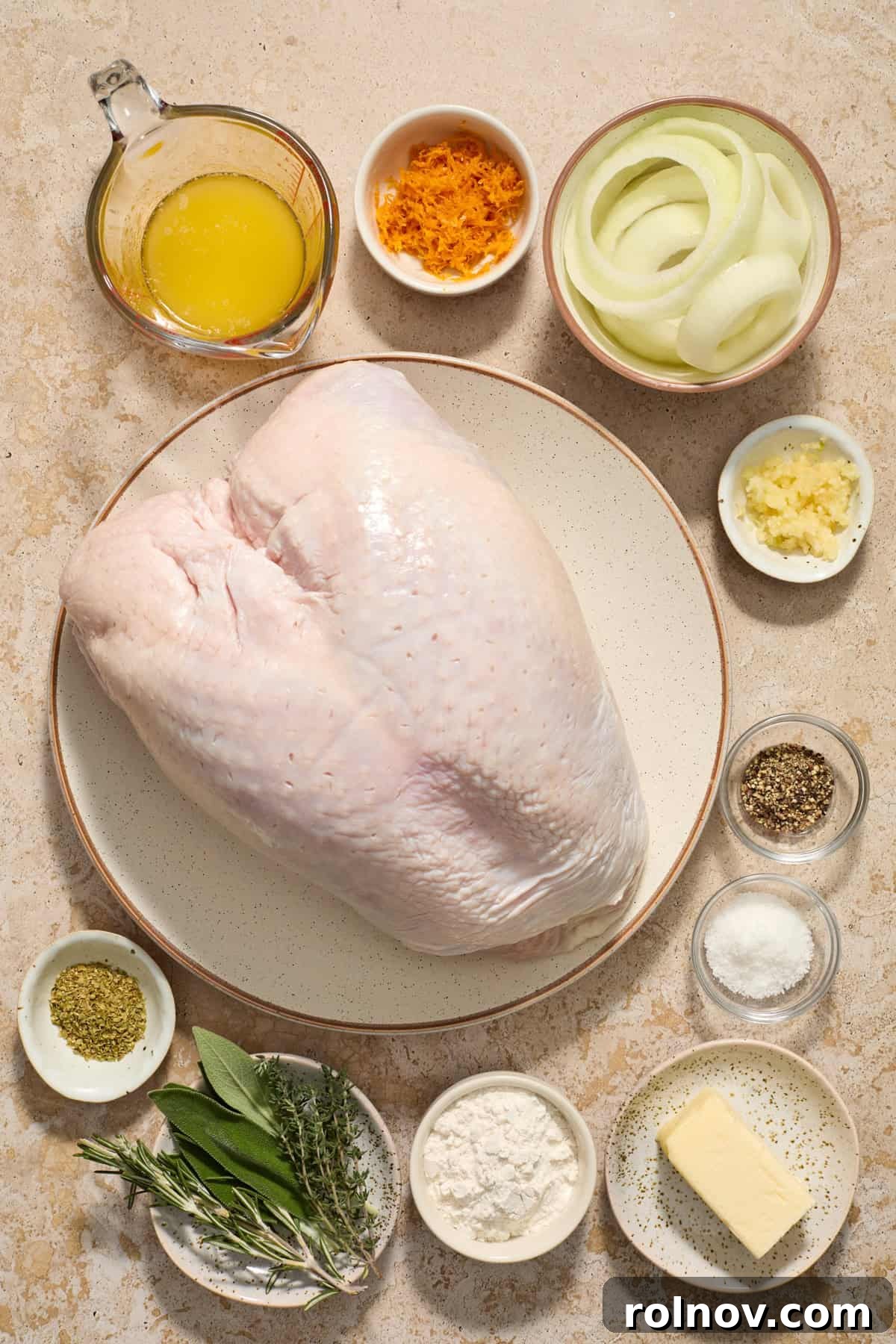 Butter, flour, herbs, orange zest, turkey breast and other ingredients arranged on surface.