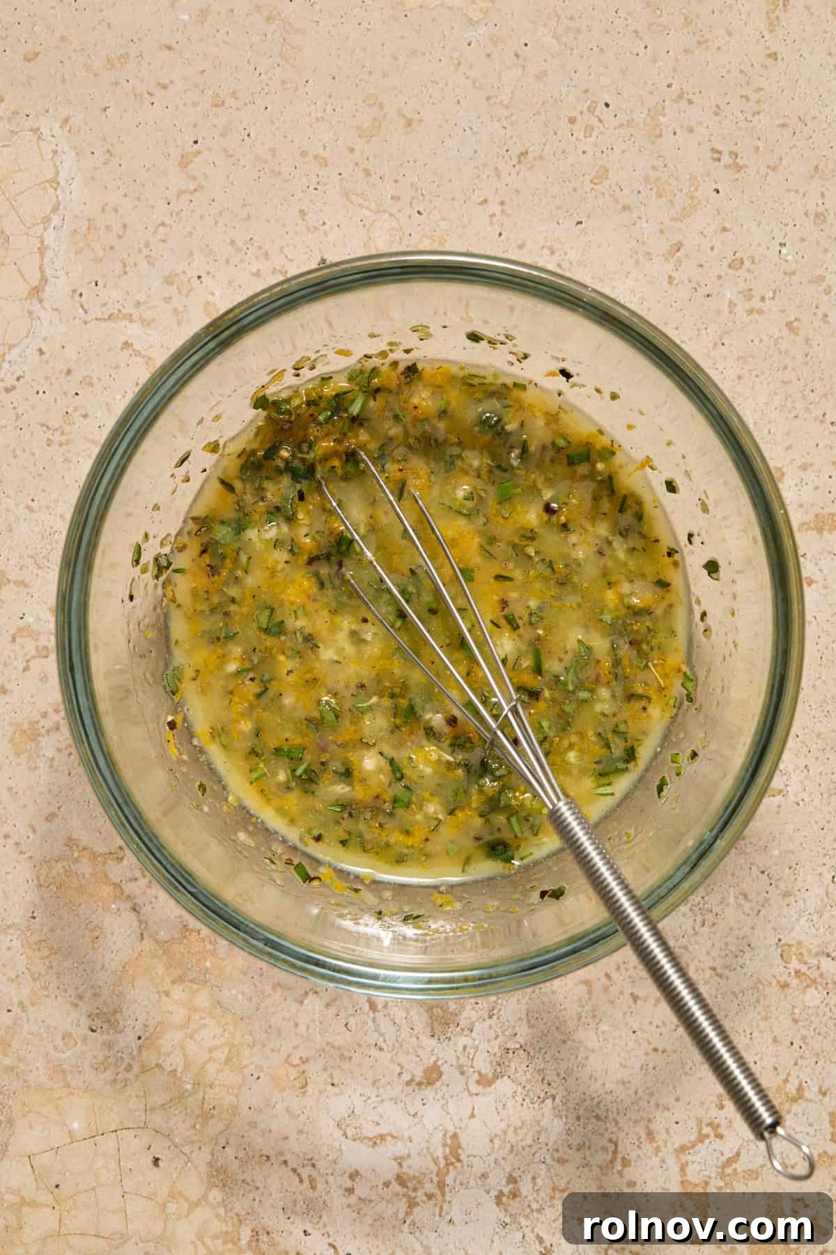 Herbs and butter whisked in small bowl with whisk propped. 