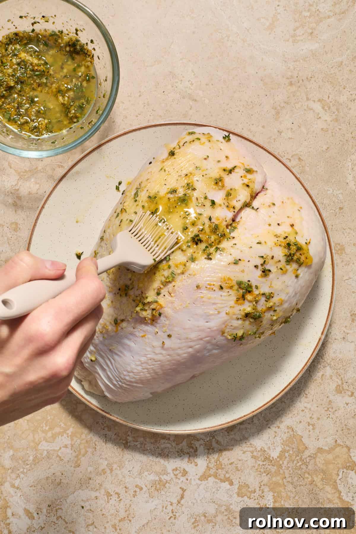 Bone in turkey breast with herb butter being brushed onto it. 