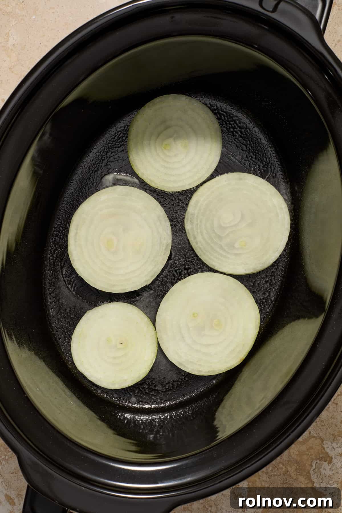 Sliced onions at the bottom of slow cooker pot.