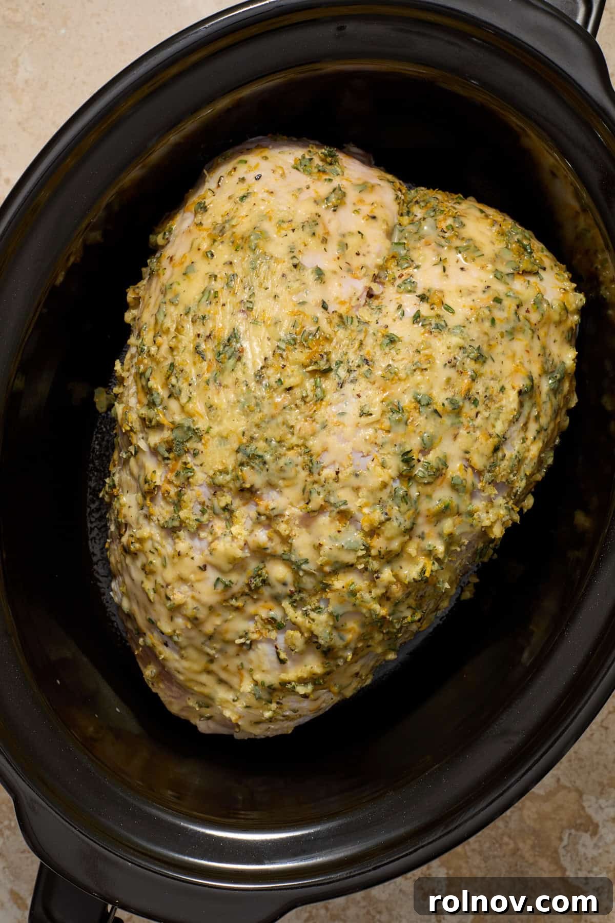 Herb and butter rubbed bone in turkey breast in slow cooker pot before cooking.