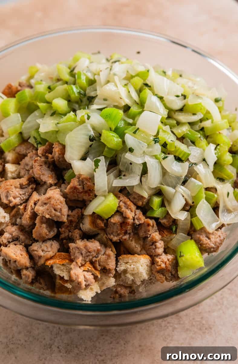 Classic Turkey Sausage Dressing 11 Sautéed celery and onion mixture being added to turkey sausage and bread in a glass mixing bowl.