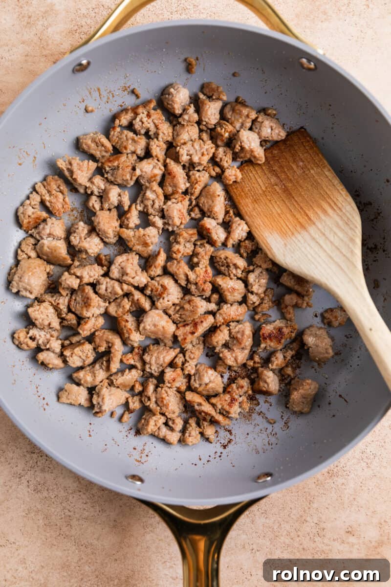 Classic Turkey Sausage Dressing 7 Browned turkey sausage in a skillet with a wooden spoon breaking up the meat.