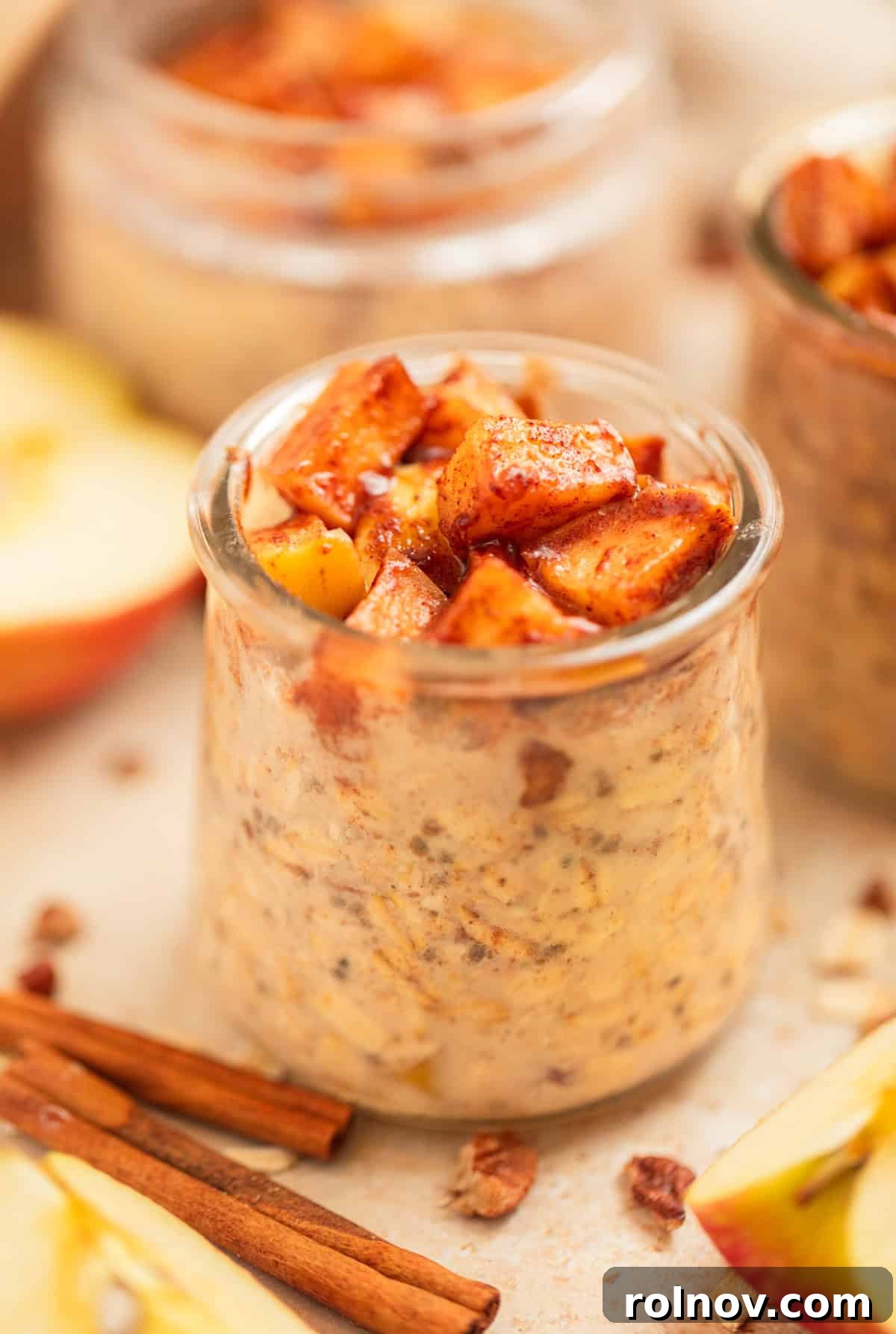 Apple Pie Overnight Oats 2 Cinnamon apple overnight oats in a jar, surrounded by fresh apples and cinnamon sticks, highlighting a comforting fall breakfast scene.
