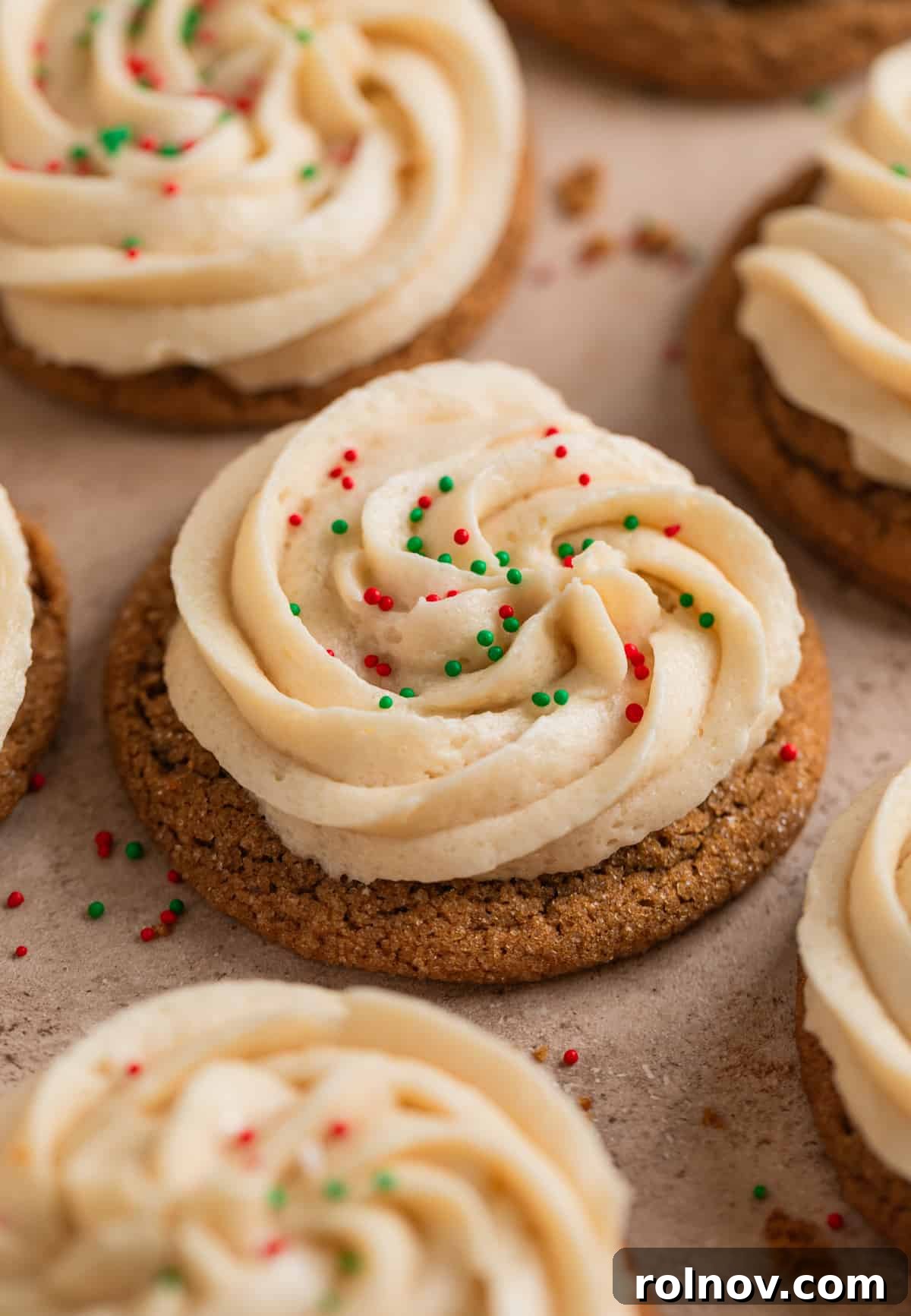 Ginger Cloud Cookies 2 Ginger cream cookies with brown sugar buttercream frosting and festive sprinkles on surface.