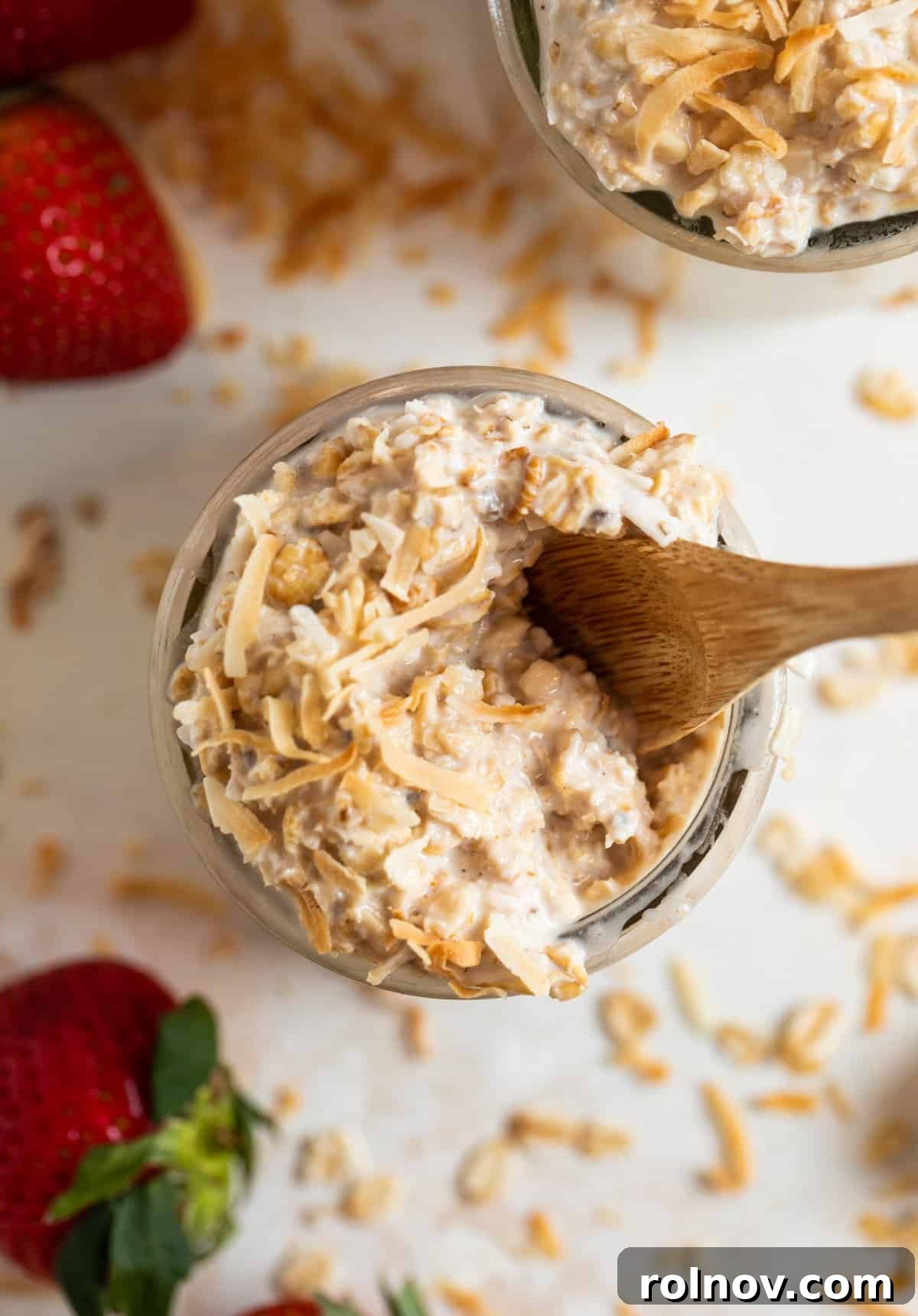 Wood spoon scooped in coconut overnight oats with oats and coconut surrounding.