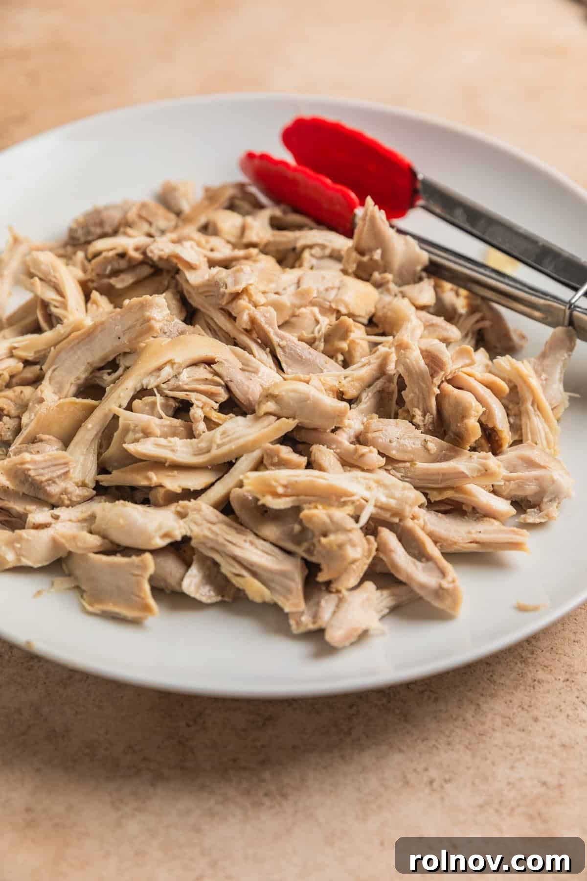 Zesty Lemon Chicken Orzo Soup 6 Succulent shredded chicken thighs arranged on a white plate, prepared with tongs, ready to be added back into the soup.