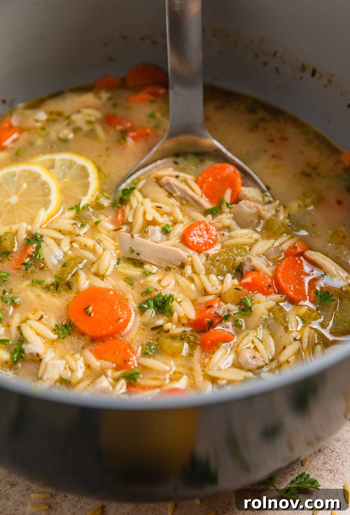 Zesty Lemon Chicken Orzo Soup 9 A ladle scooping a generous portion of lemon orzo soup with chicken from a large pot, showcasing its hearty ingredients.