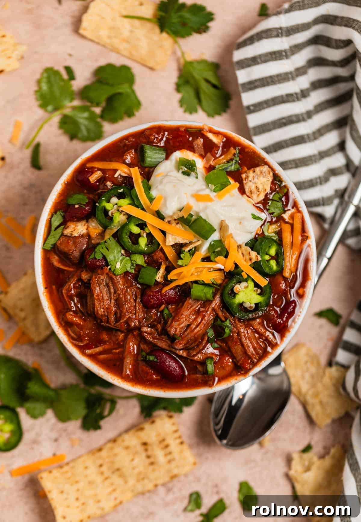 Slow Cooker Pulled Beef Chili 12 Overhead view of a hearty bowl of chili, generously topped with cool sour cream, shredded cheese, fresh cilantro, and other delicious garnishes.