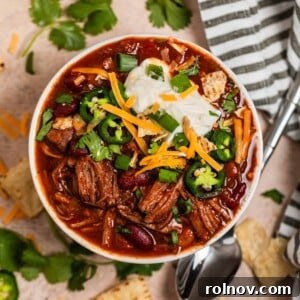 Overhead view of shredded beef chili topped with sour cream, cilantro, cheese and more.