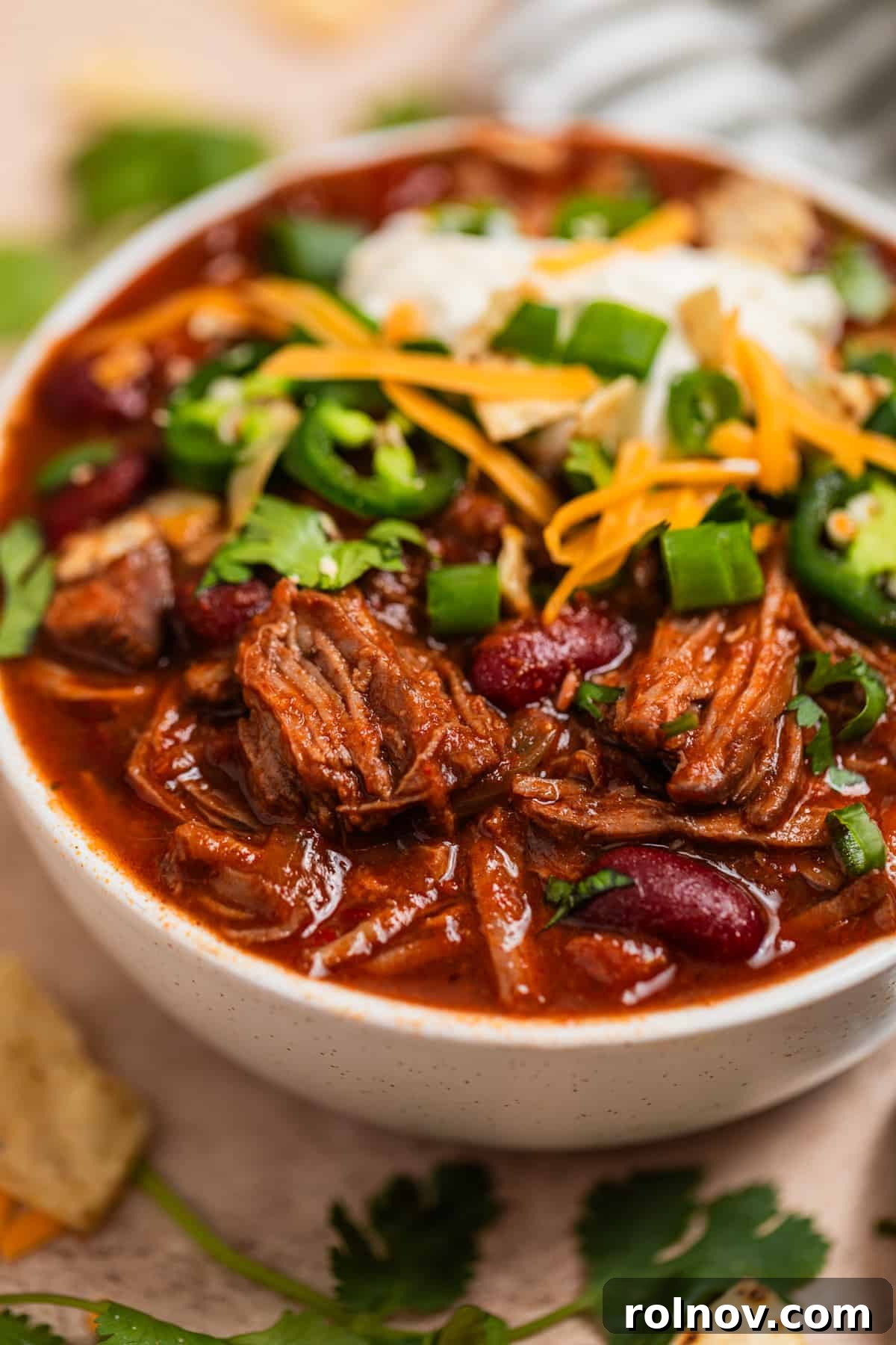 Slow Cooker Pulled Beef Chili 3 A vibrant bowl of crockpot chili, generously topped with a dollop of cool sour cream, a sprinkle of sharp cheddar cheese, and other fresh toppings, ready to be enjoyed.