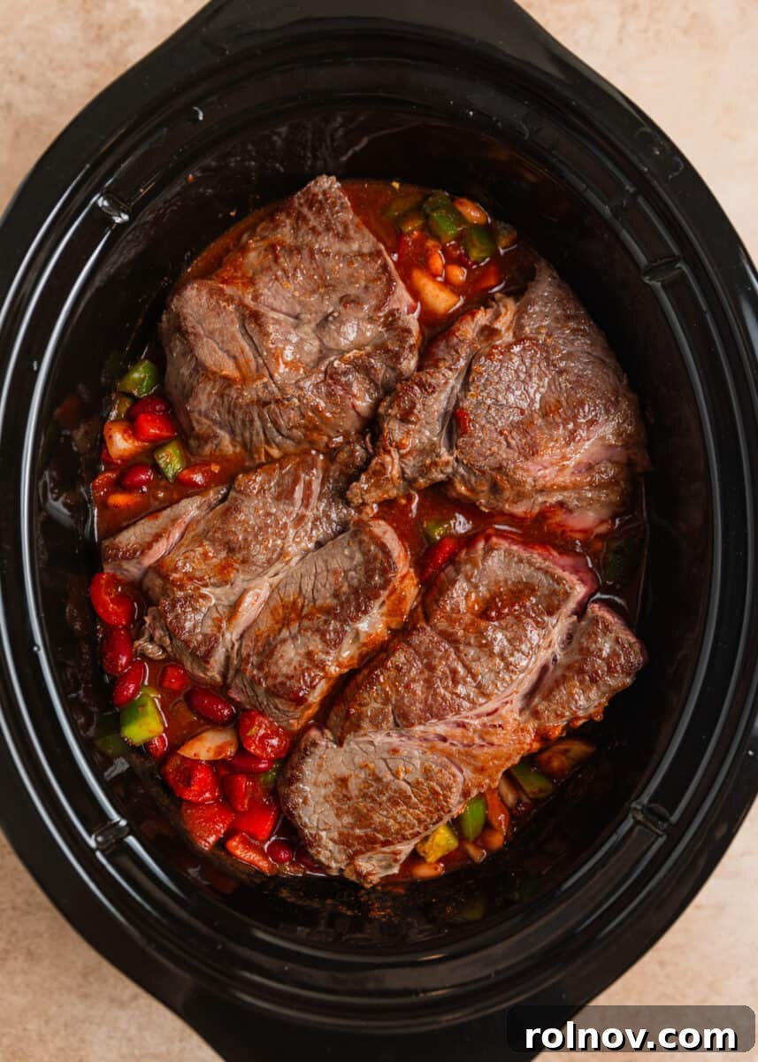 Slow Cooker Pulled Beef Chili 7 Seared chuck roast chunks carefully placed on top of the mixed chili ingredients inside the slow cooker, ready for the slow cooking process.