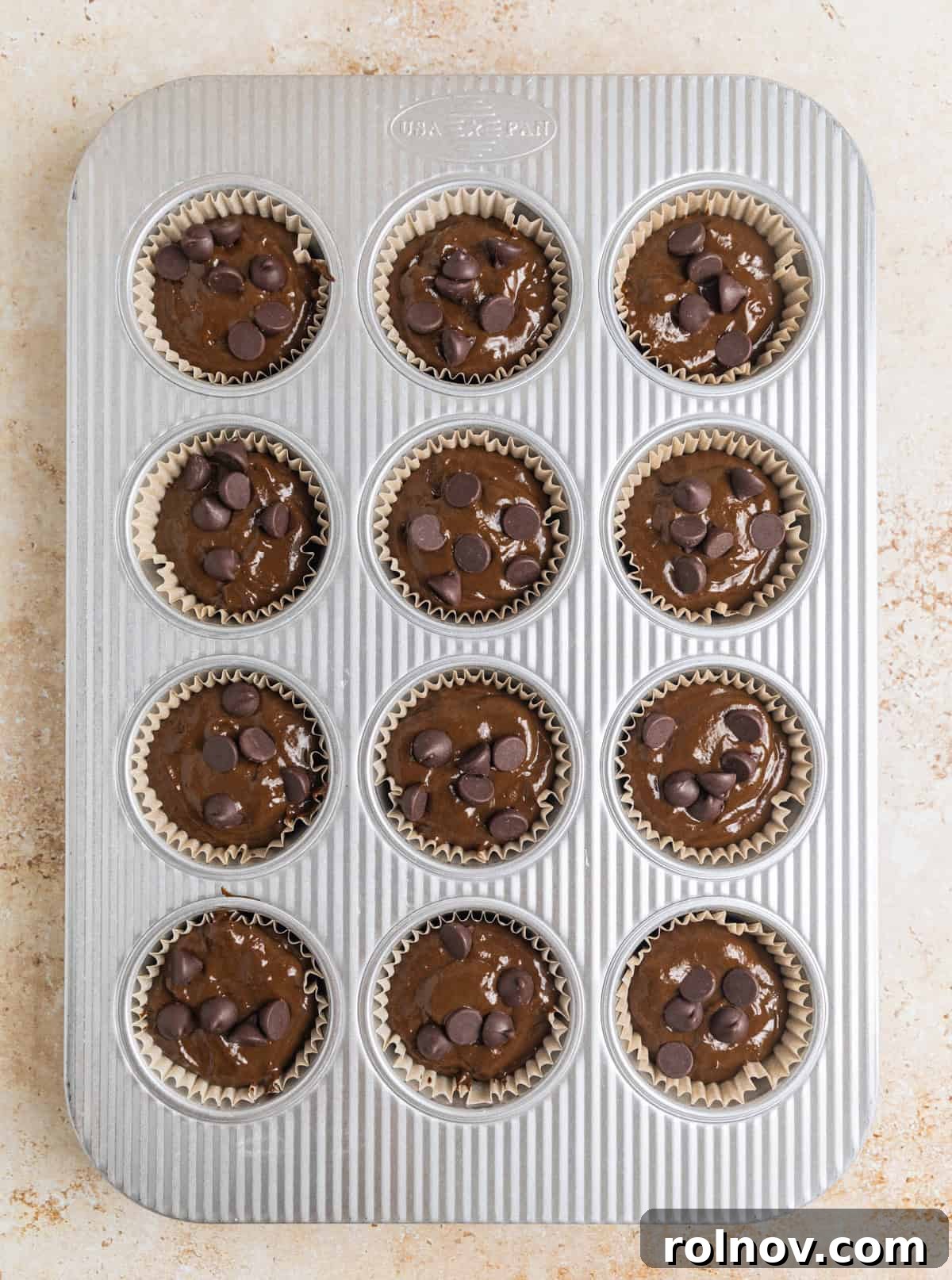 Emerald Chocolate Muffins 12 Muffin batter scooped in muffin pan with chocolate chips on top.